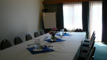 A conference room with a long table, chairs, a projector screen, and a window with curtains.