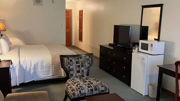 A hotel room with a bed, a sofa, a chair, a table, a dresser, a television, and a microwave.