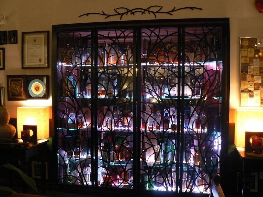 Een kamer met een glazen vitrine gevuld met verschillende flessen en ingelijste certificaten aan de muur.