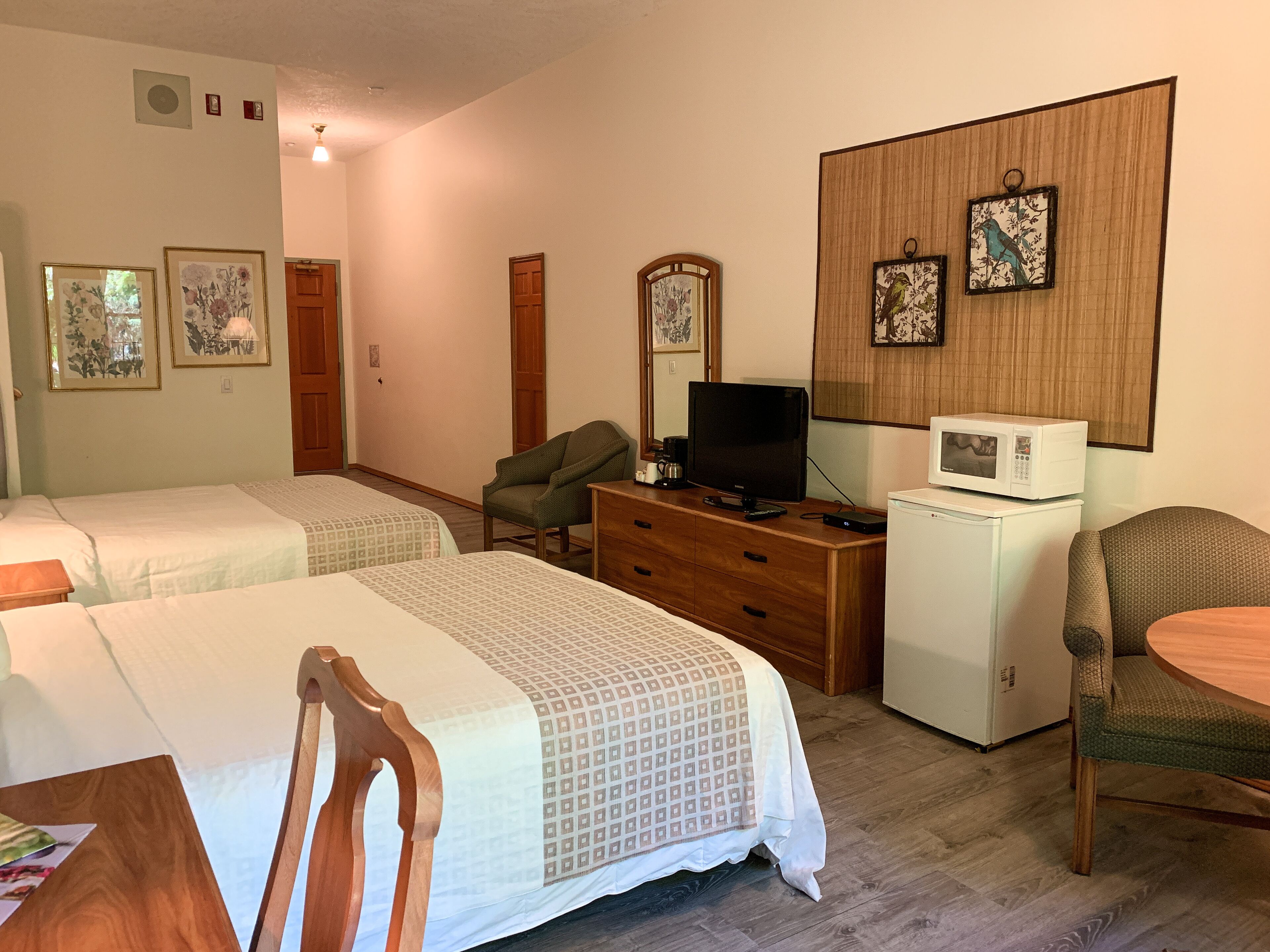 A hotel room with two beds, a wooden dresser, a television, a microwave, and two chairs.