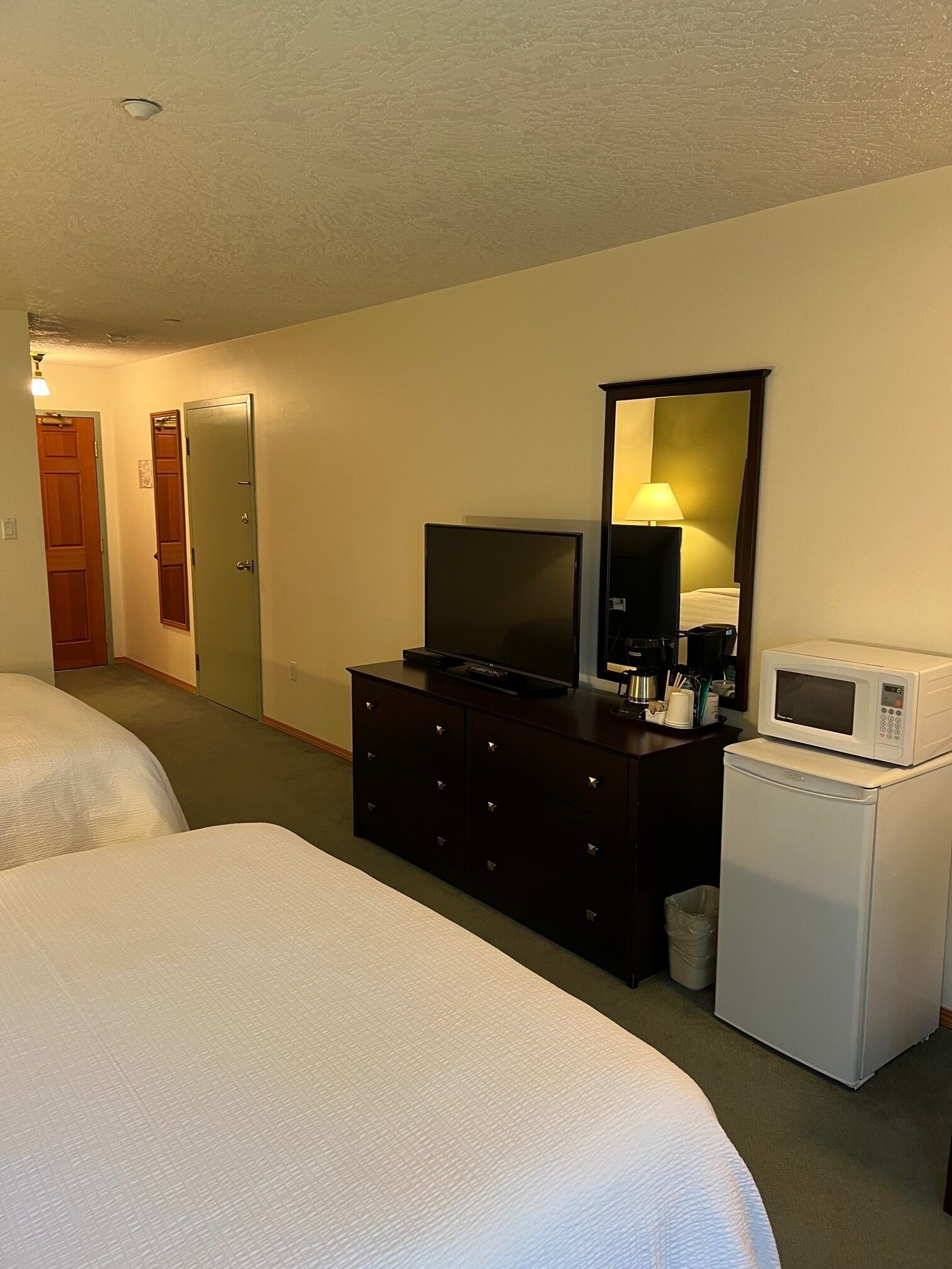 A hotel room with two beds, a dresser with a TV and microwave, a small trash bin, and a mirror on the wall.