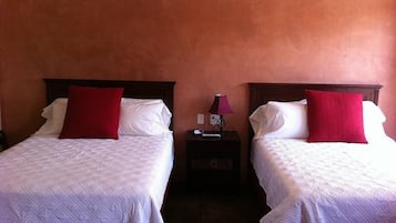 Two beds with white linens and red pillows, a nightstand with a lamp, and a wall with a textured finish.