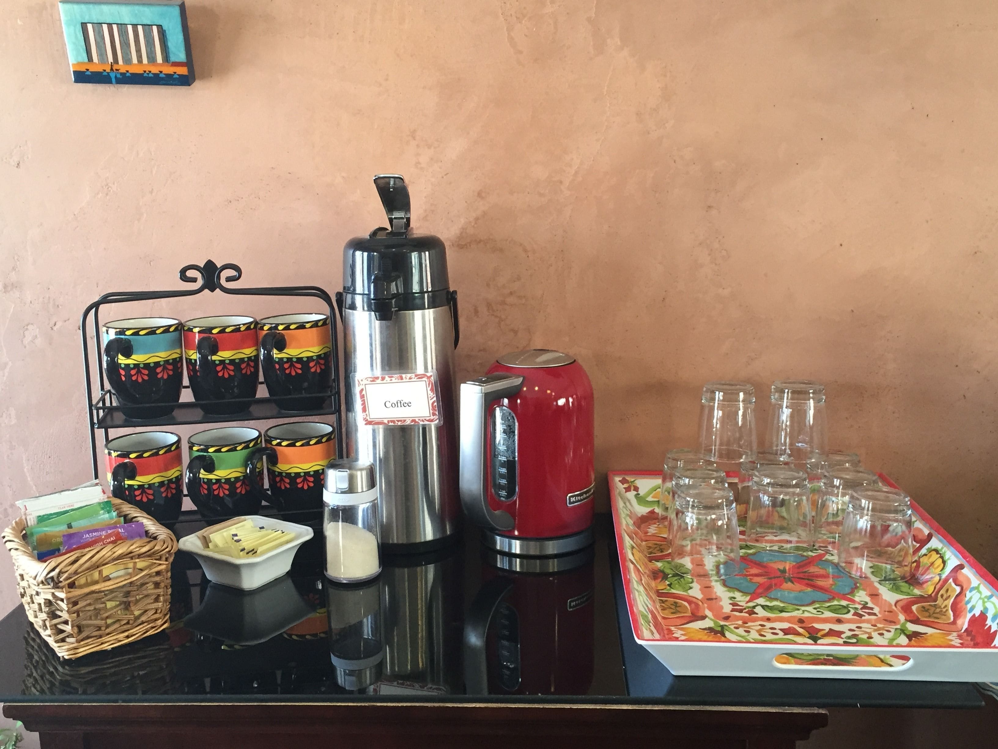 A coffee station with a coffee maker, cups, and a tray of glasses.