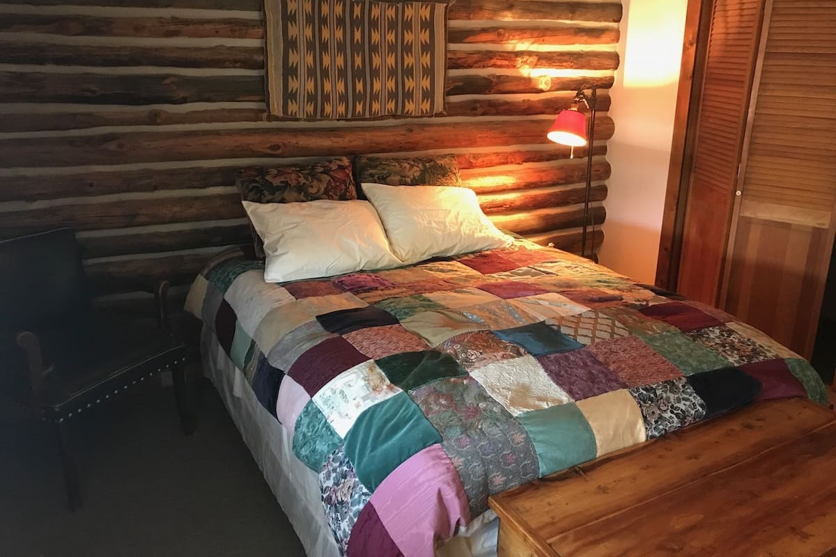 Un dormitorio de estilo cabaña con edredón acolchado, un banco de madera y una lámpara.