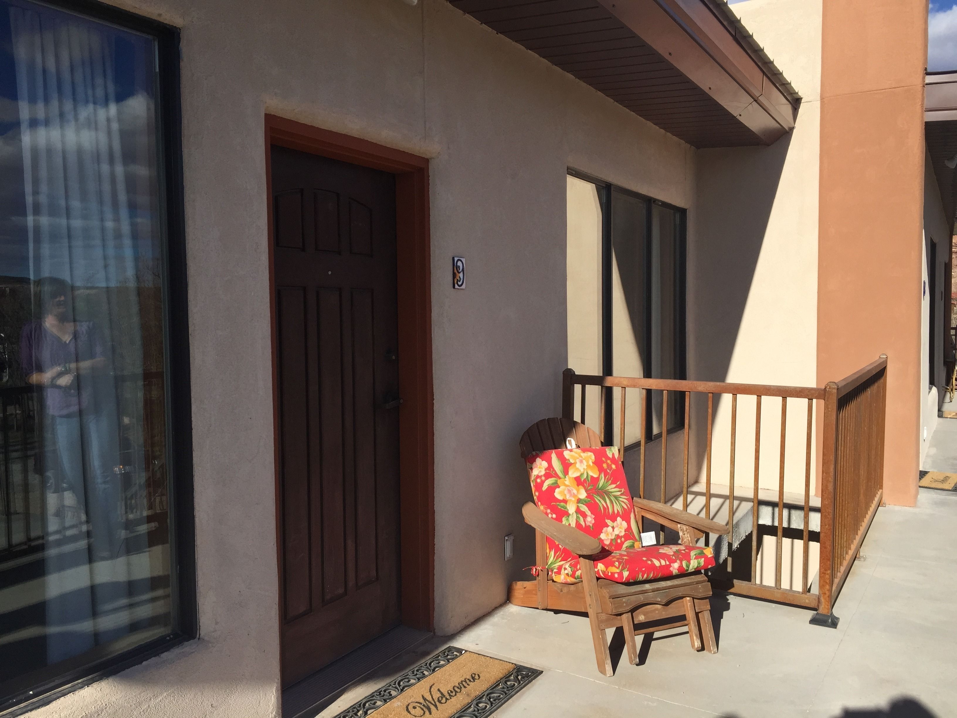 A wooden chair outside a building with a closed door and a window.