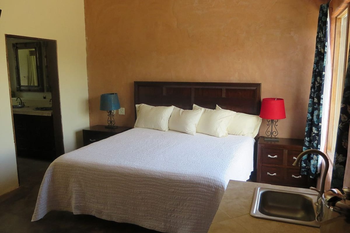 Un dormitorio con cama, lámparas de noche, mesita de noche, espejo y ventana con cortinas.