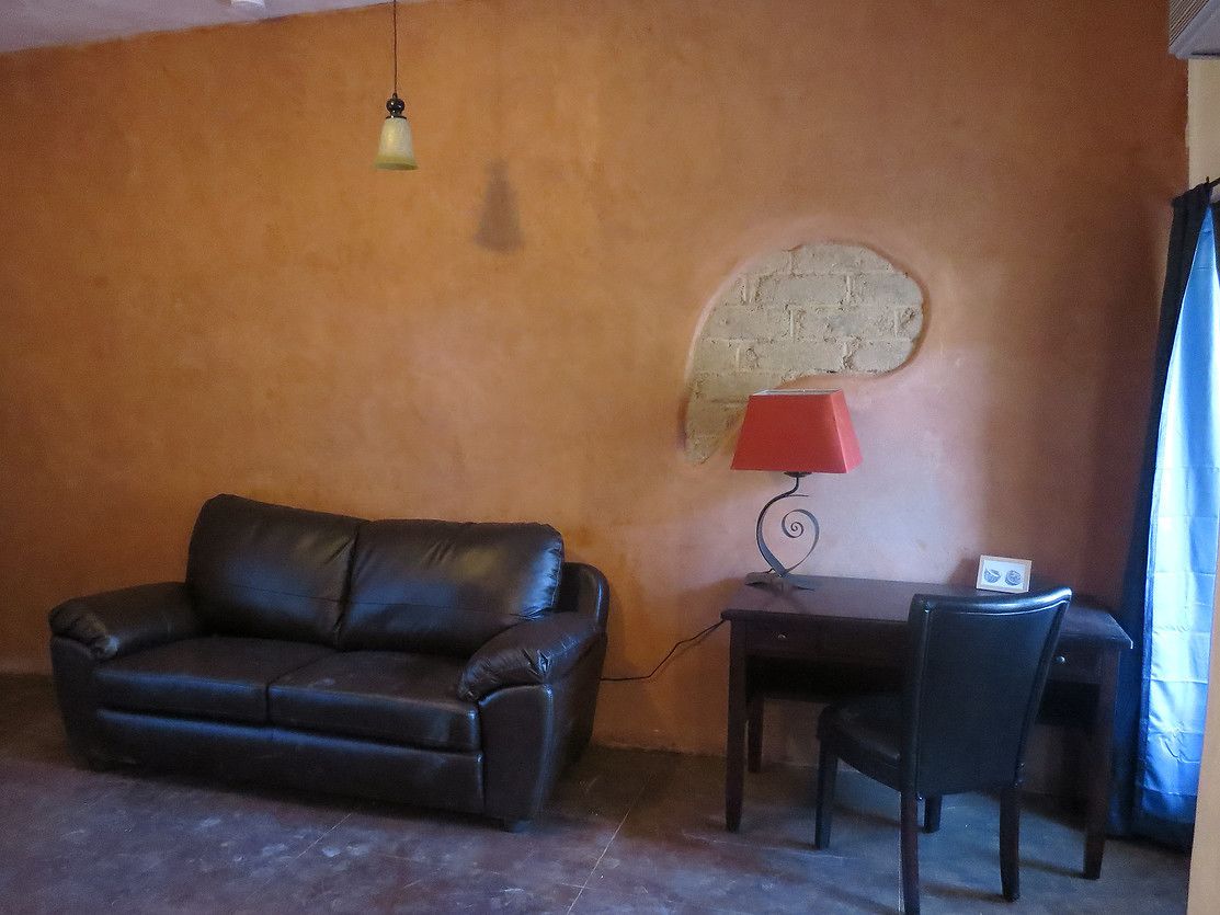 A room with a black leather sofa, a small table with a red lamp, and a chair.