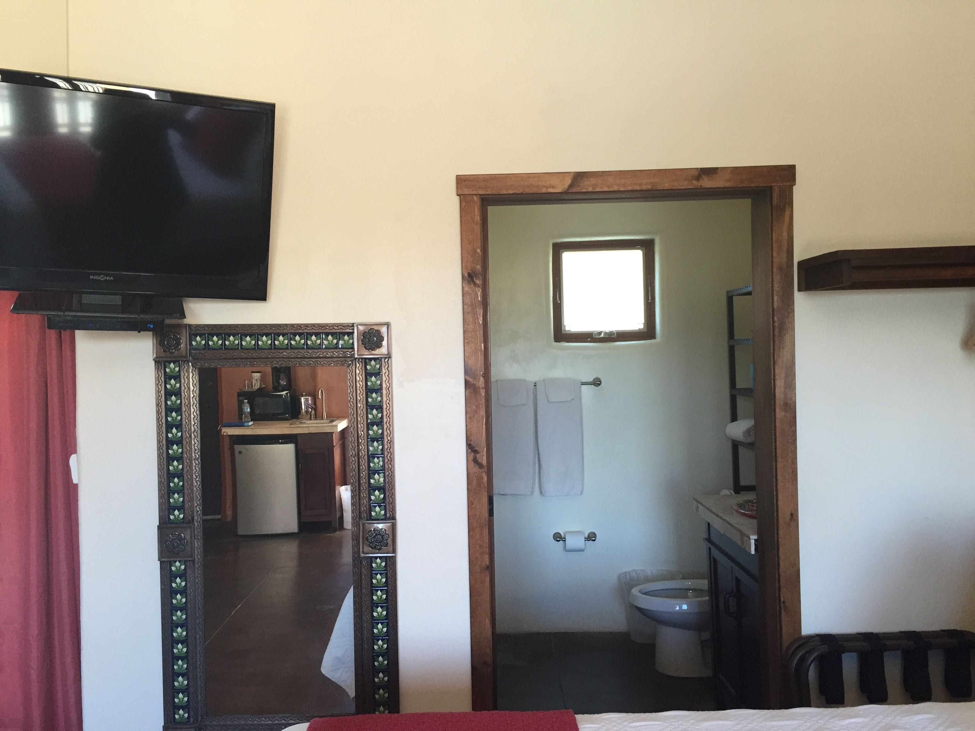 A room with a bed, a TV mounted on the wall, a bathroom with a toilet and sink, and a small window.