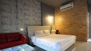 Habitación de hotel con cama blanca, sofá rojo y pared de ladrillo.