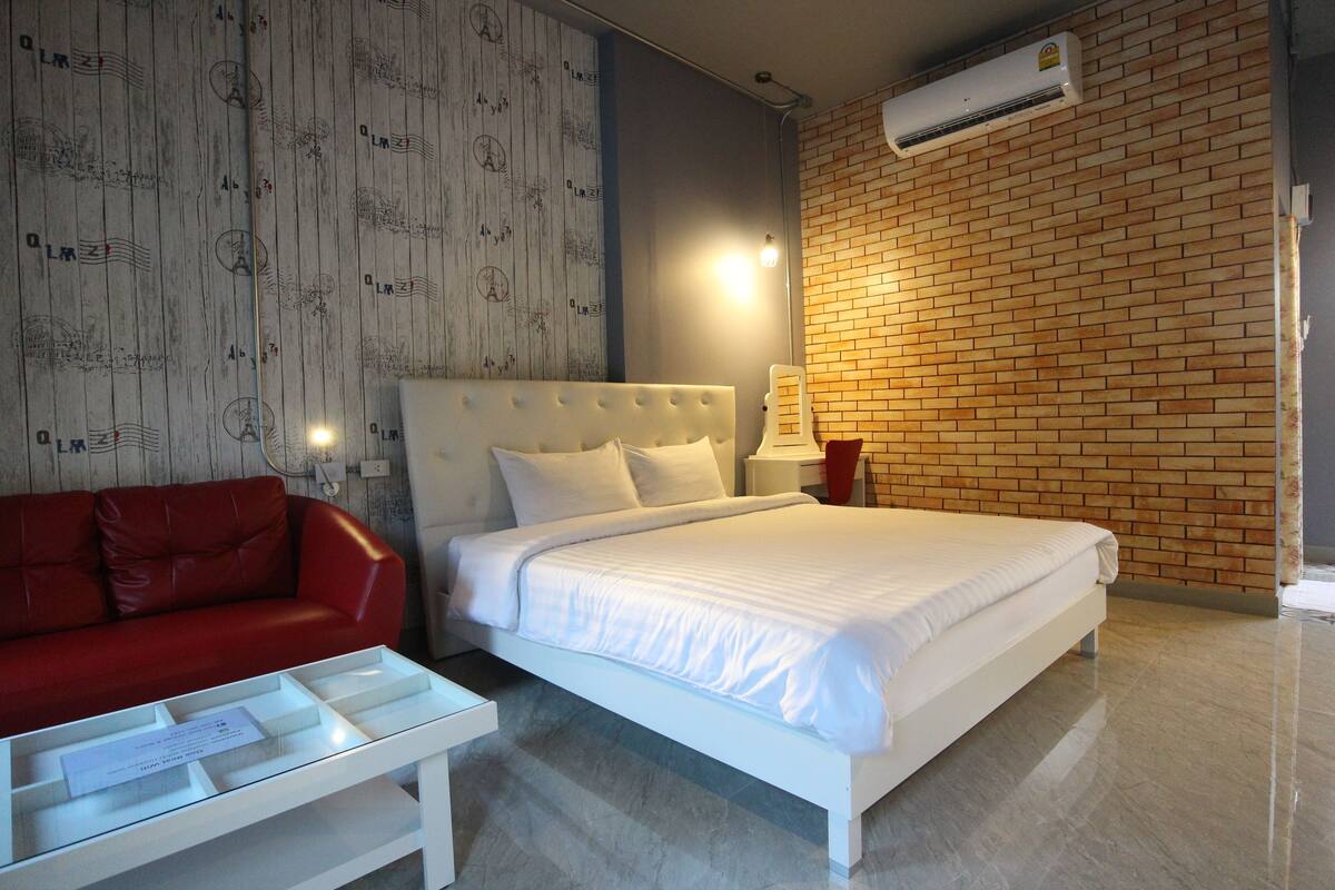 Habitación de hotel con cama blanca, sofá rojo y pared de ladrillo.