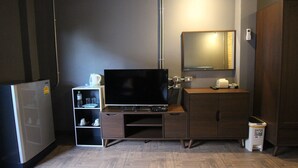 Habitación de hotel compacta con televisión de pantalla plana, un refrigerador pequeño, un armario de madera, un espejo y un cubo de basura.