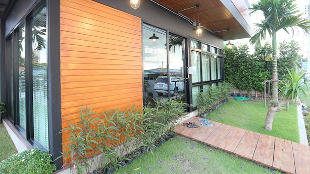 Un edificio moderno con ventanas amplias, fachada de madera y un pequeño jardín con terraza de madera.