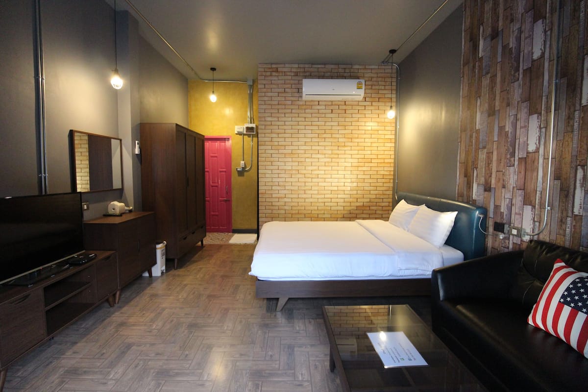 Una habitación de hotel con cama, televisión, cómoda, espejo y pared con diseño de ladrillo.