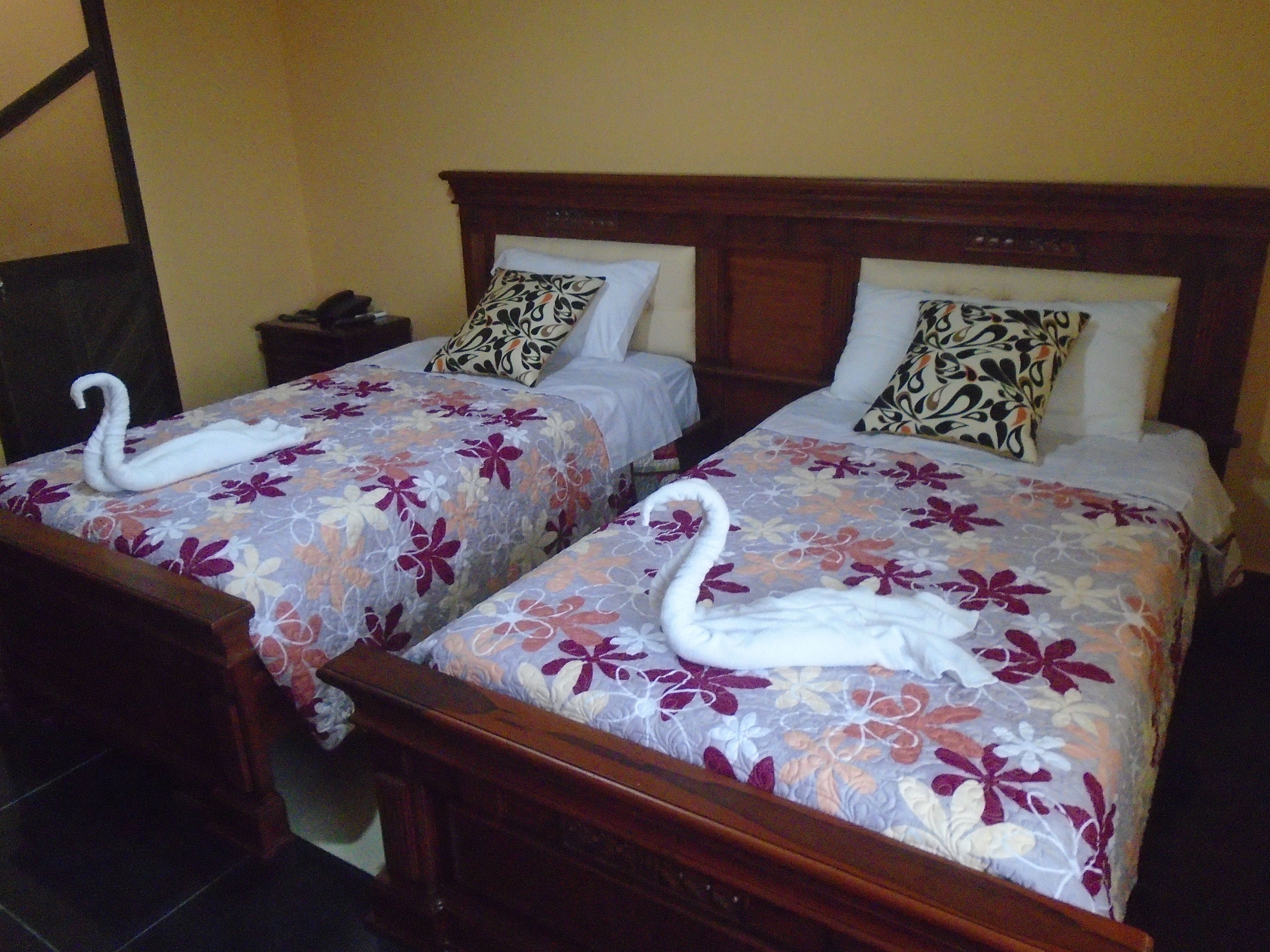 Una habitación de hotel con dos camas, cada una con ropa de cama floral y toallas decorativas con forma de cisne.