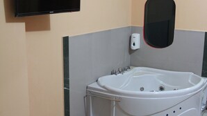 A bathroom with a large bathtub, a mounted TV, and a wall-mounted mirror.