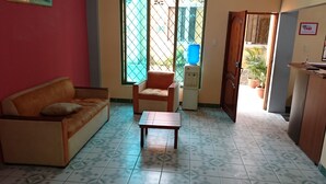 A room with a sofa, a chair, a small table, a water dispenser, and a door leading to another area. - Platinum Class Hostal (Nueva Loja)