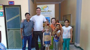 A family posing in a hallway with a sign for Platinum Class Hospital and a door with a 'BAÑO' sign.