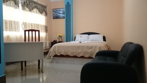 A hotel room with a bed, a desk, a chair, a vase with flowers, and a picture on the wall. - Platinum Class Hostal (Nueva Loja)