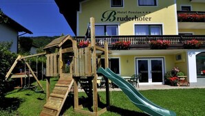 A wooden play structure with a slide in front of a hotel named 'Hotel Pension Bruderhofer'. - Pension Bruderhofer (ALTMUENSTER)