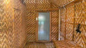 A room with a woven bamboo ceiling and walls, a metal door, and a woven floor.