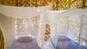 Two beds with canopy beds in a room with a woven wall and a view of a cityscape.