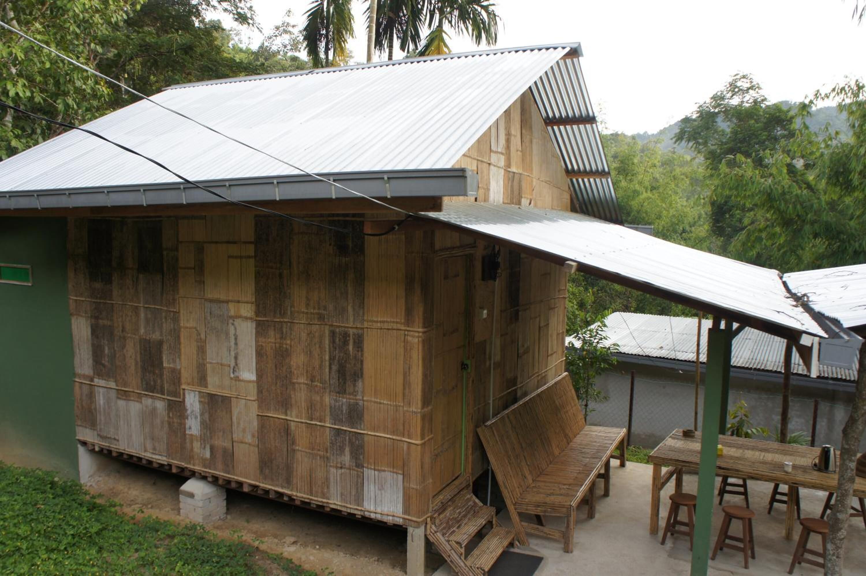 A rustic wooden structure with a metal roof, a small porch with a table and chairs, and a surrounding natural landscape.
