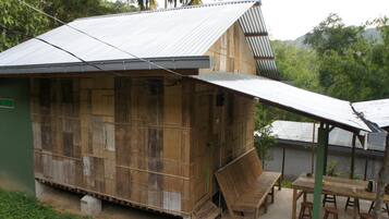 A rustic wooden structure with a metal roof, a small porch with a table and chairs, and a surrounding natural landscape.