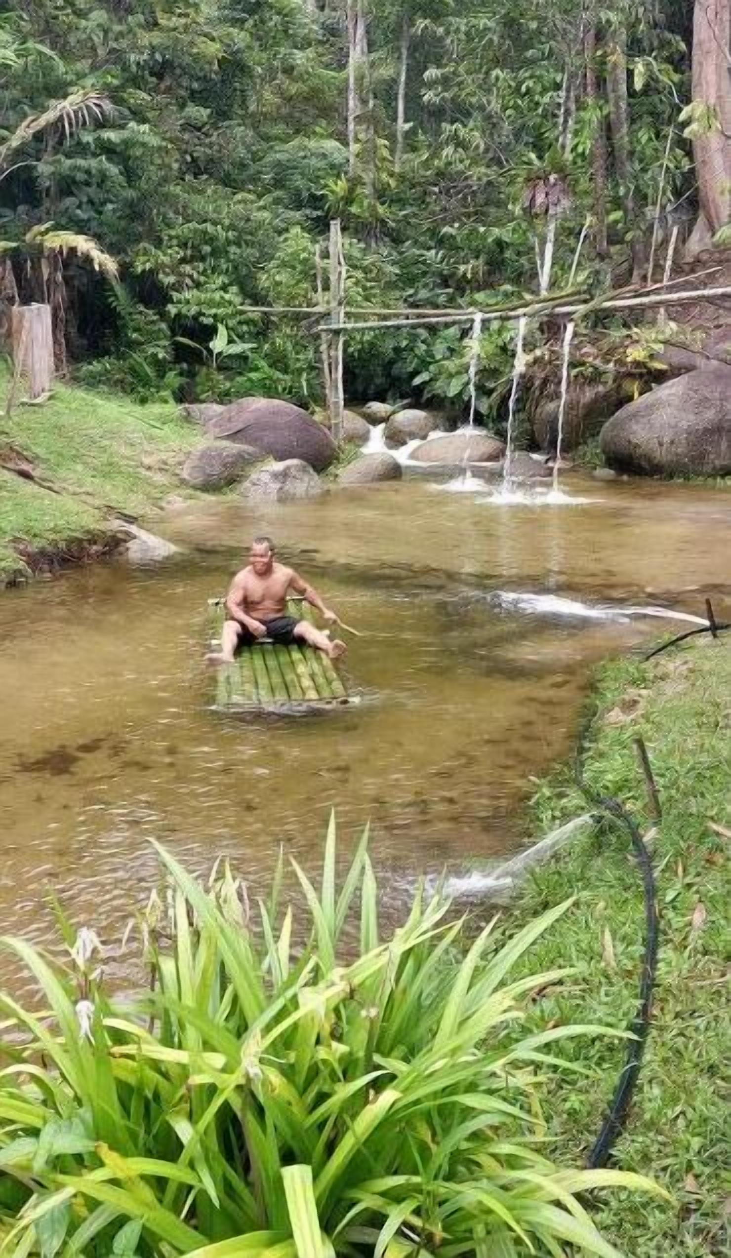 Une personne assise sur une plateforme flottante, au milieu d’un plan d’eau naturel, entourée de végétation et de rochers.