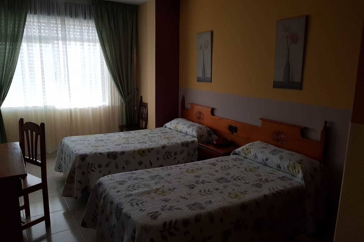 A hotel room with two beds, a wooden headboard, a small table, and a chair.