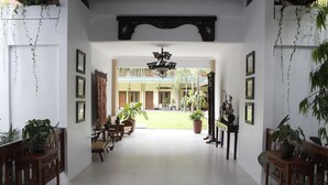 A spacious hallway with a central open area, wooden furniture, potted plants, and framed pictures on the walls.