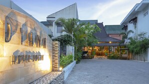 A hotel entrance with a stone wall displaying the name "Diana Hotel" and a paved courtyard with a traditional gazebo.