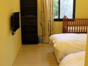 Una habitación pequeña con dos camas, un armario, un televisor y una ventana con cortinas.