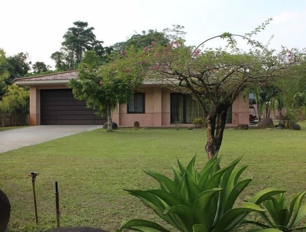 Una casa residencial con garaje, césped y un árbol con flores rosadas.