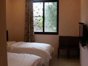 Una habitación con dos camas, un ventanal con vistas a follaje y un banco.