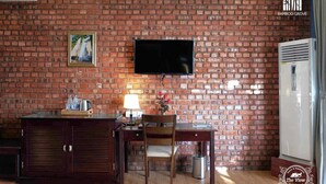 Une pièce avec un mur en briques, un téléviseur à écran plat fixé au-dessus d’un bureau en bois, une chaise et un meuble.