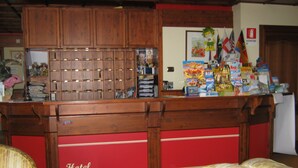 Een receptiebalie met een houten toonbank, een rood gedeelte onderin, en een bordje met de tekst 'Hotel Belvedere'.