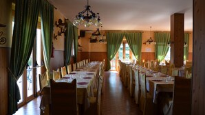 Een lange eetzaal met meerdere gedekte tafels, houten wanden en een kroonluchter.