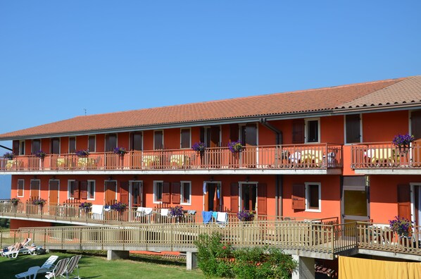 Un hotel de varios pisos con balcones, mobiliario exterior y un cielo azul despejado.