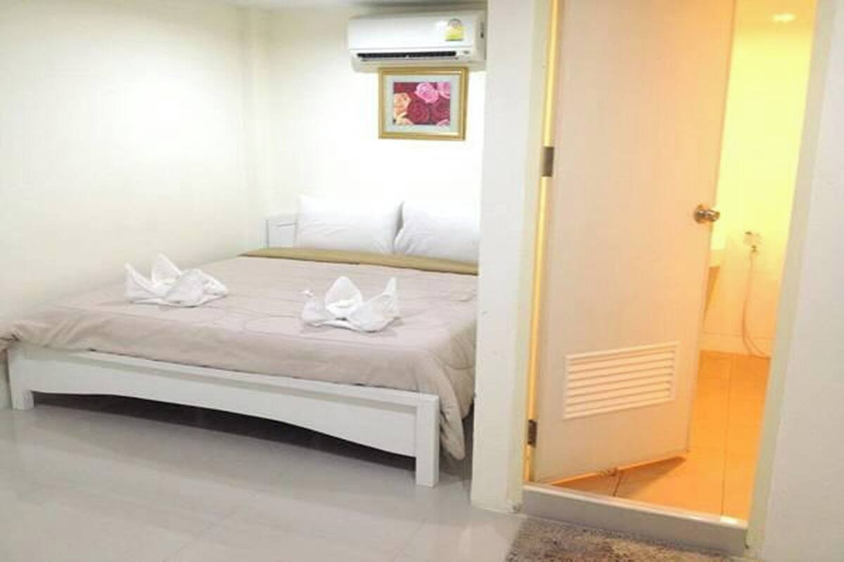 A bedroom with a bed, a bedside table, an air conditioning unit, and a door leading to a bathroom.
