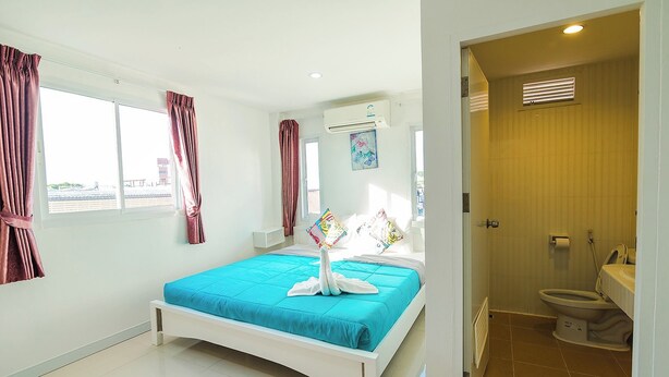 A hotel room with a bed, a window with curtains, an air conditioning unit, a bathroom with a toilet, and a shower area. - Bird Hotel (Chonburi)