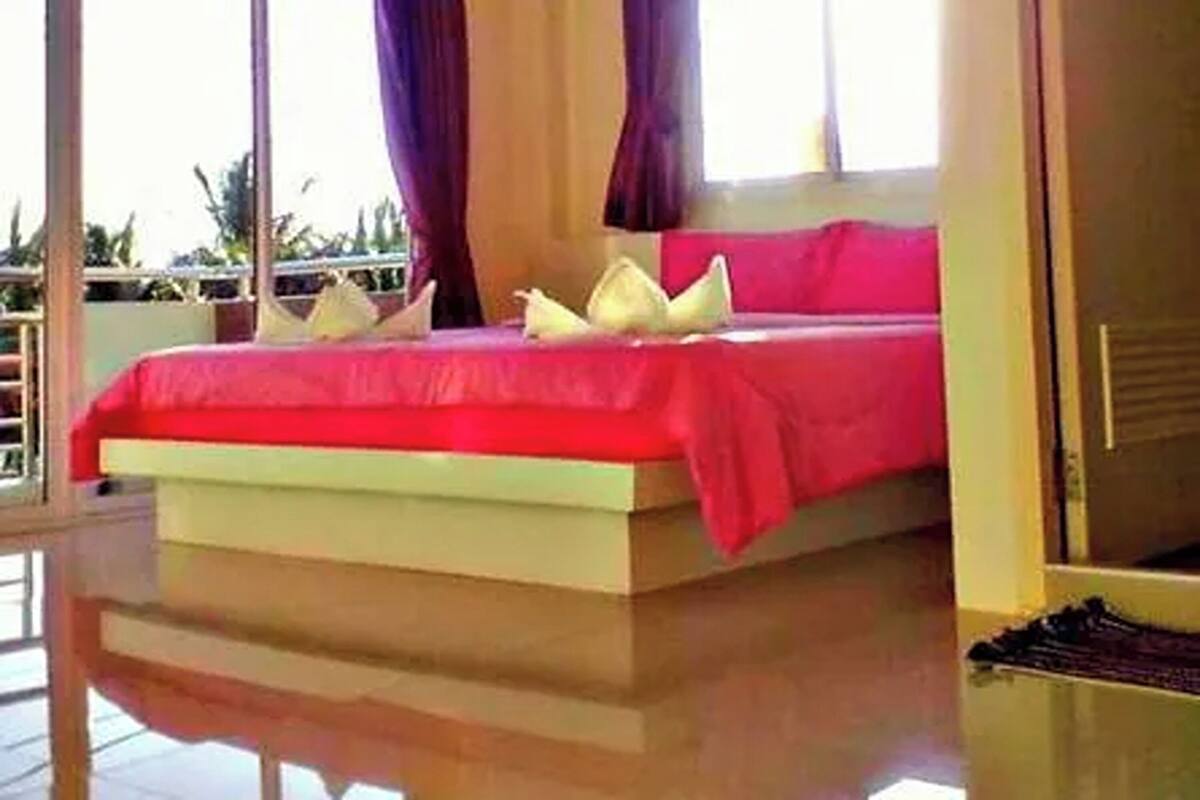 A bedroom with a large bed, a window with curtains, and a view of greenery outside.