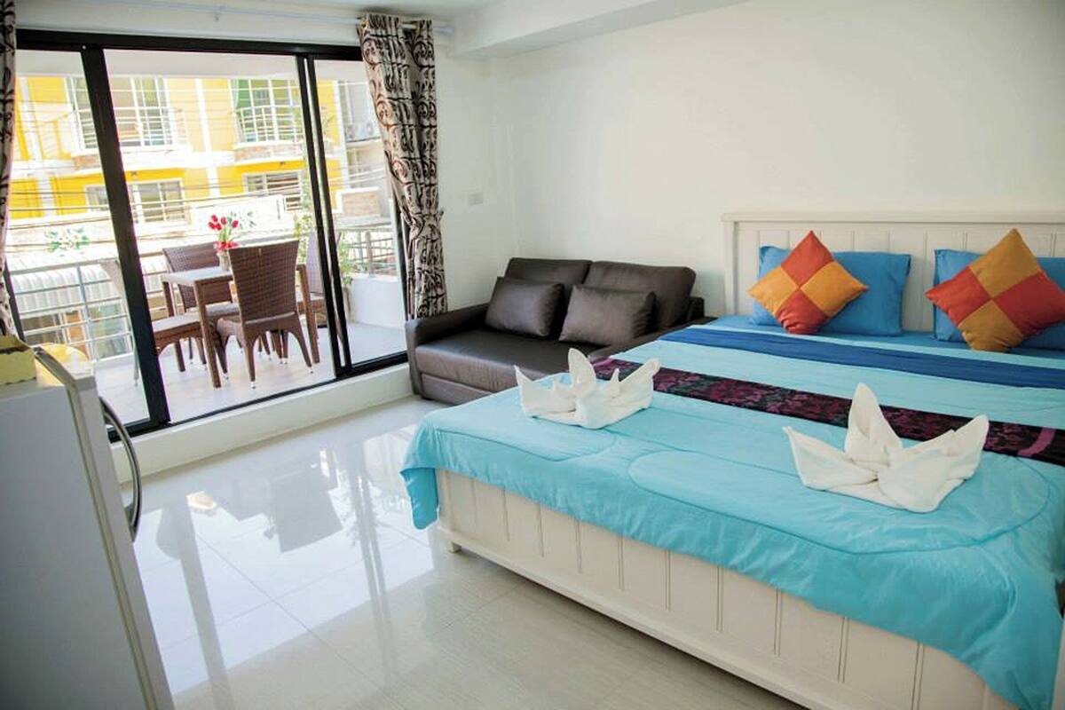 A hotel room with a balcony, a sofa, a bed with a blue bedspread, and a white headboard.