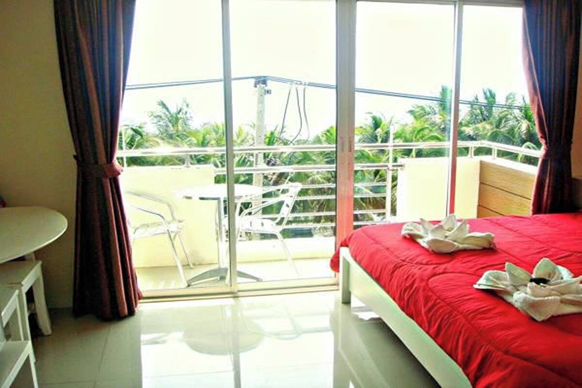 A hotel room with a balcony, a bed with a red bedspread, and a table with chairs.