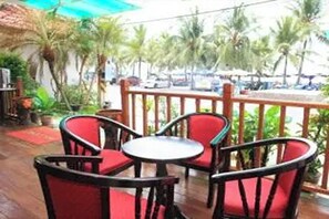An outdoor seating area with red chairs and a round table, surrounded by a wooden railing. - Bird Hotel (Chonburi)