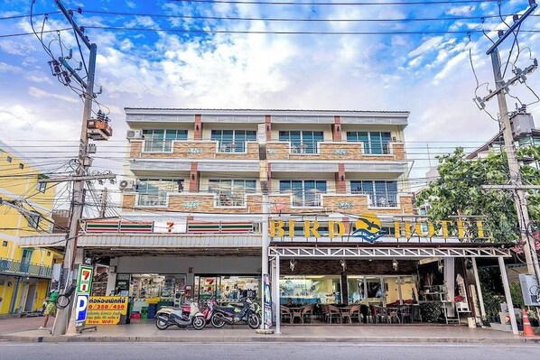 A hotel with a 7-Eleven convenience store on the ground floor, outdoor seating, and a signboard. - Bird Hotel (Chonburi)