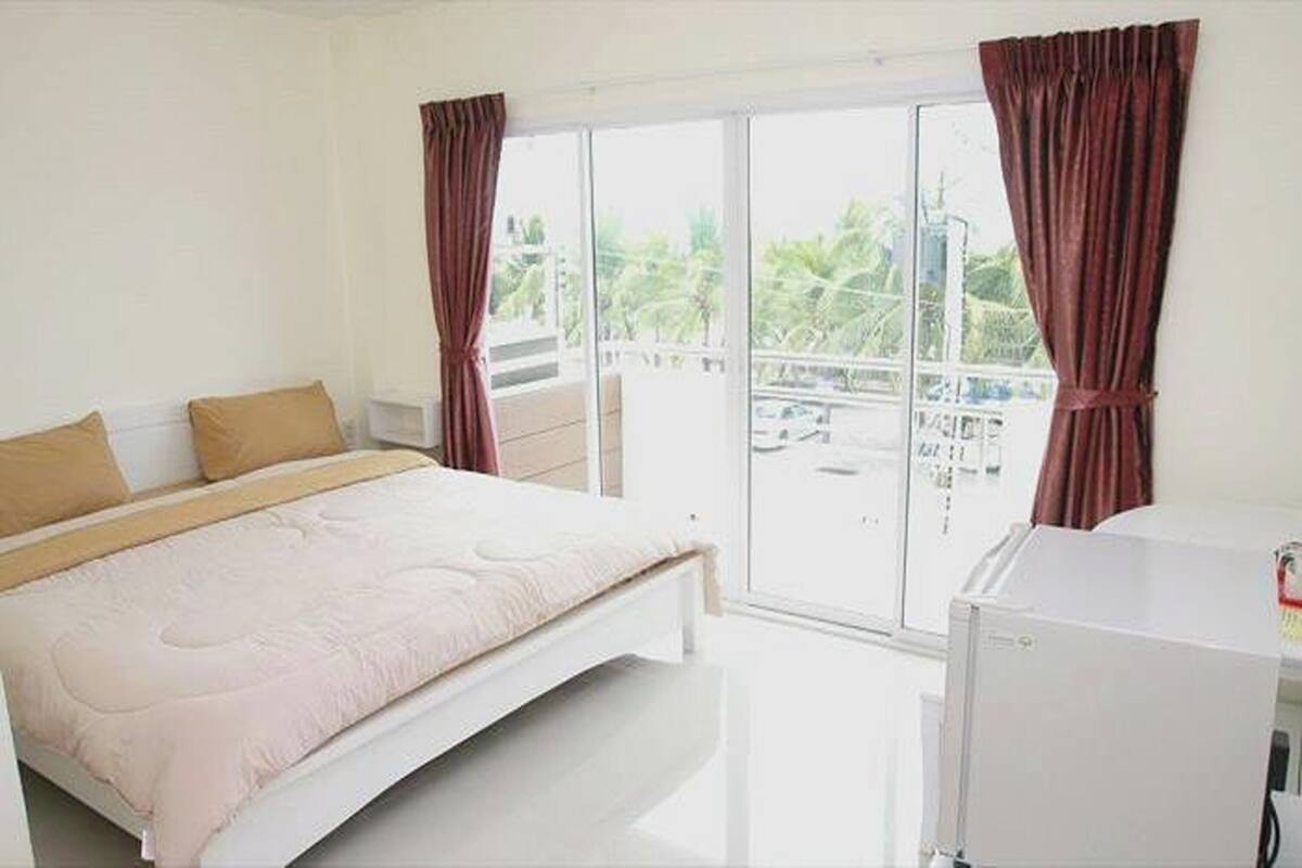 A bedroom with a bed, a window, and a refrigerator.