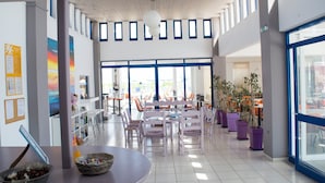 A spacious indoor area with a high ceiling, multiple tables and chairs, and large windows allowing natural light. - Bouradanis (Kos)