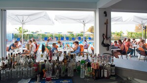 An outdoor dining area with tables and chairs, a pool in the background, and various bottles and glasses on the tables. - Bouradanis (Kos)
