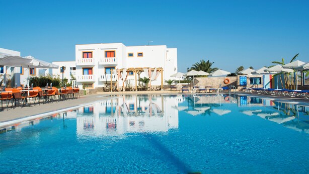 A clear blue swimming pool with lounge chairs and umbrellas, surrounded by white buildings with orange accents. - Bouradanis (Kos)