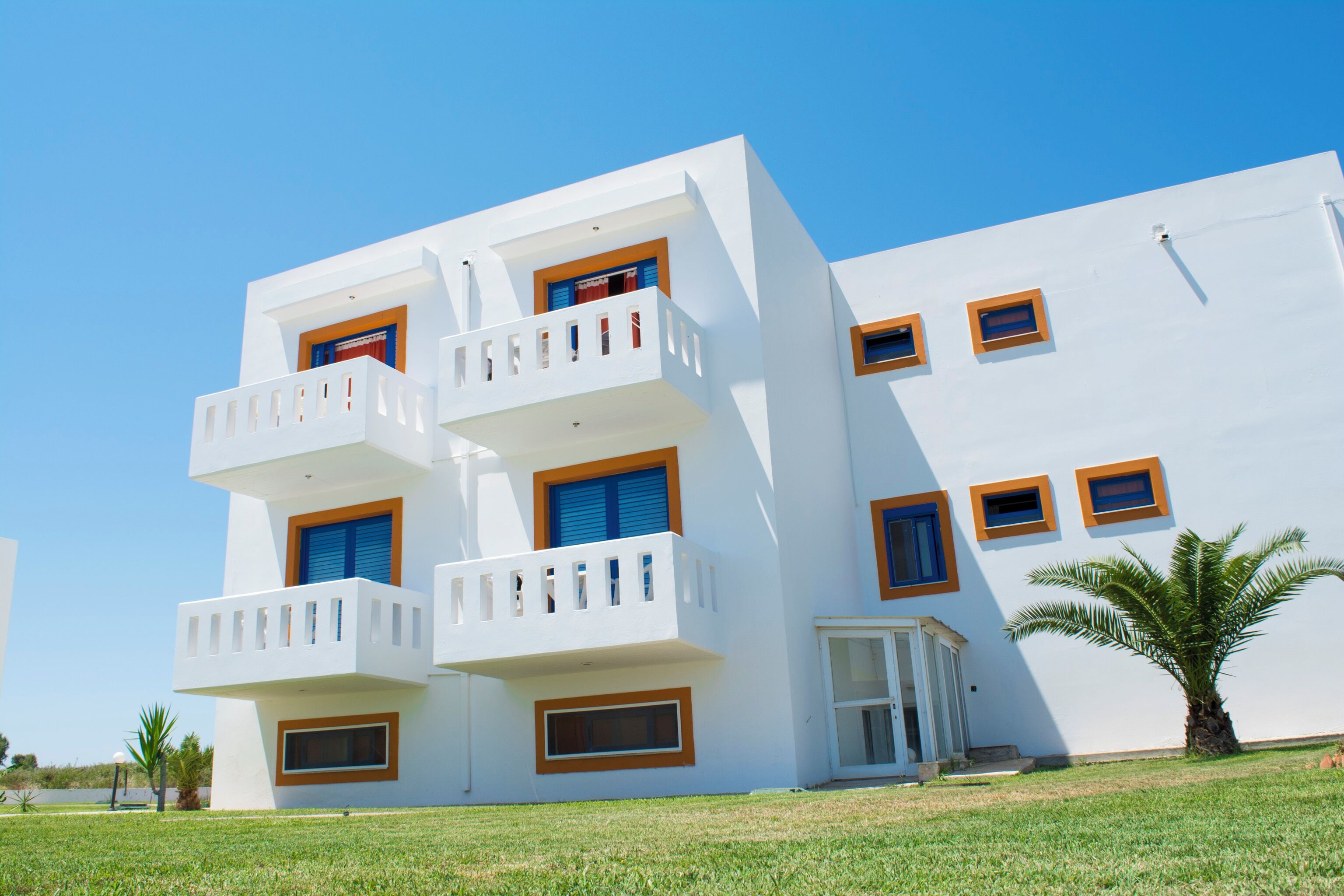 A modern multi-story building with balconies, a flat roof, and a clear sky.